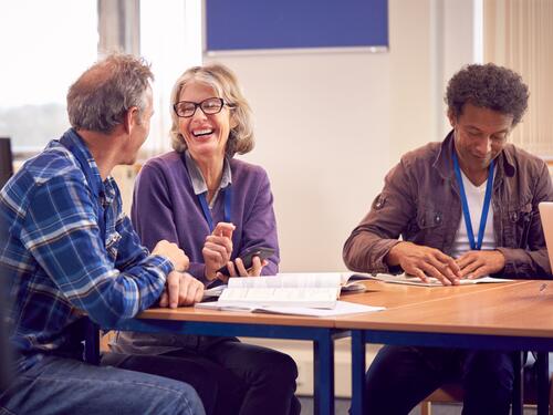 Teacher With Mature Female Adult Student Using Mobile Phone At Table Working In College Library