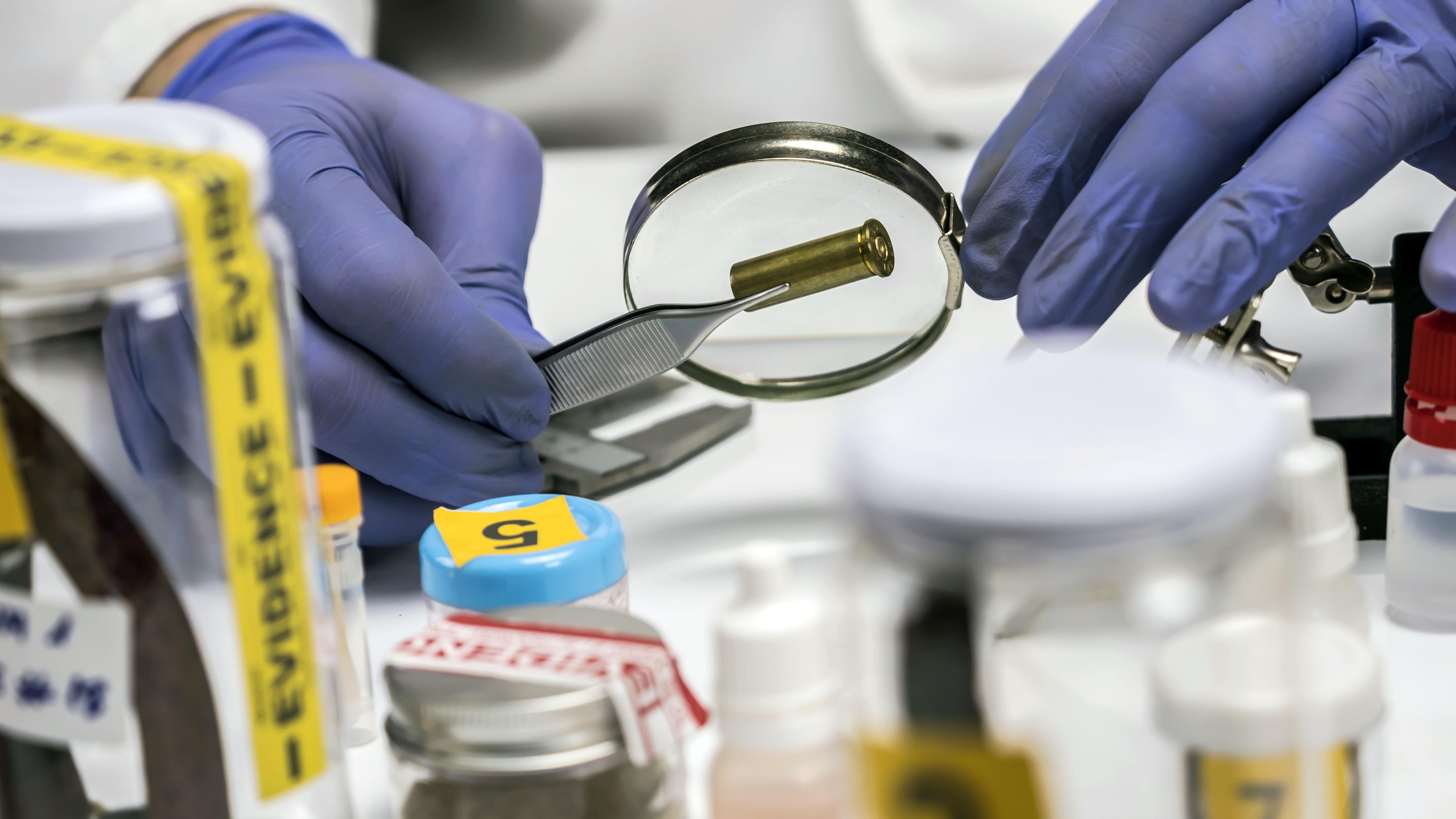 Expert police examines a bullet cap in scientific laboratory with magnifying glass